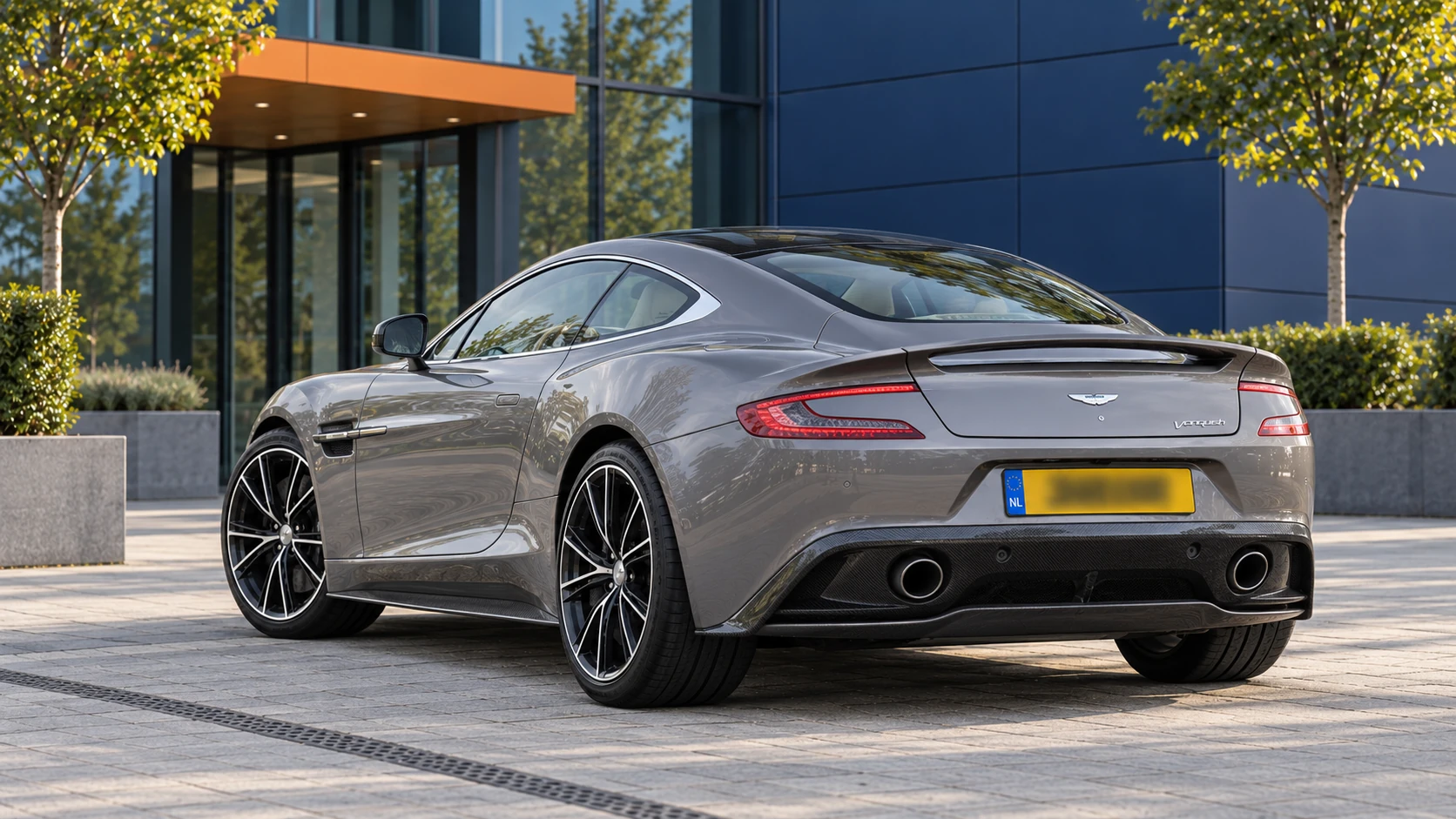 Grijze eerdere Aston Martin Vanquish Coup&eacute; van achteren met twee ronde uitlaten