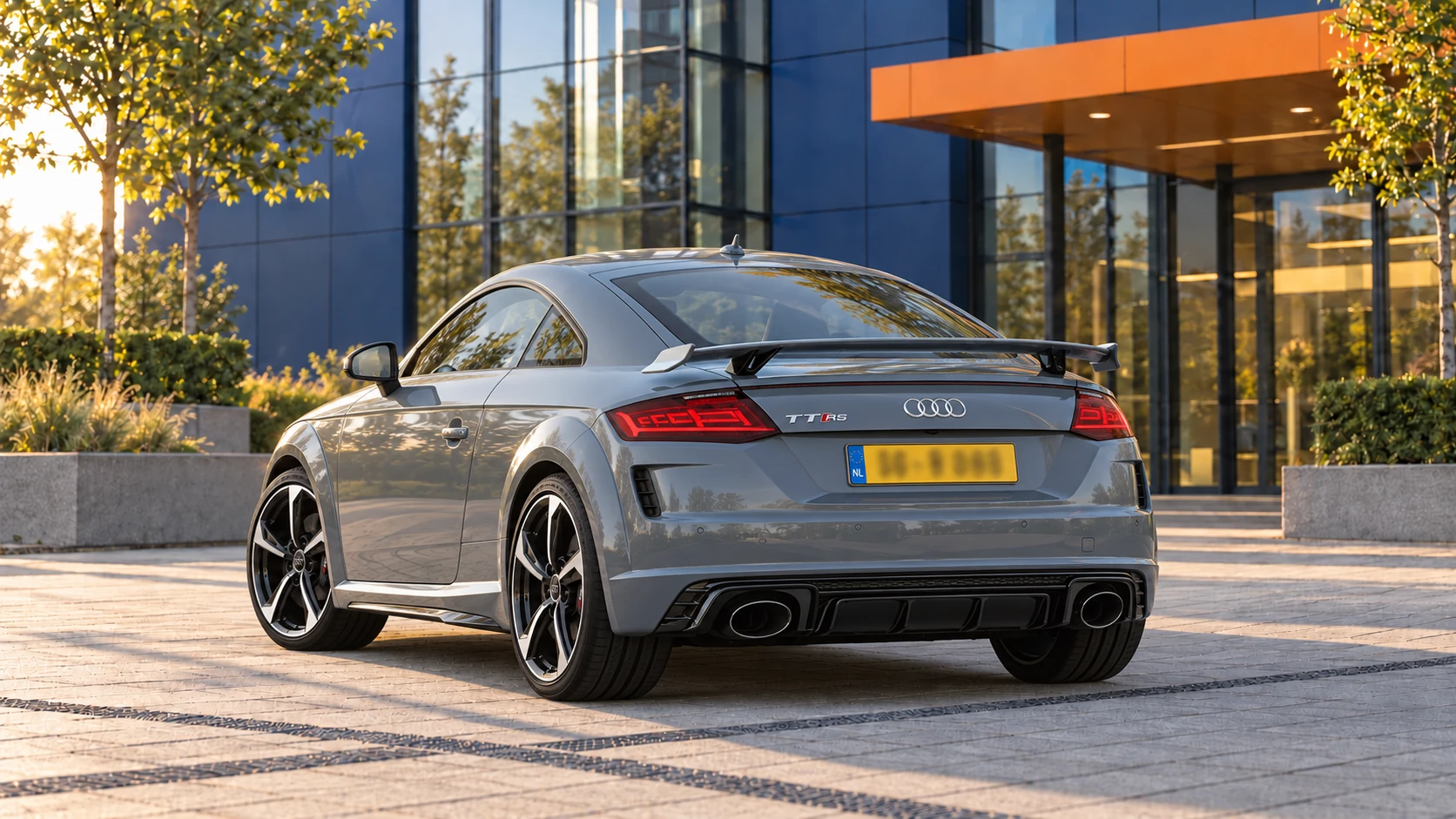 Grijze Audi TT RS Coup&eacute; van de 8S faceliftgeneratie, schuin van achteren met vaste achterspoiler en twee grote ovale uitlaten