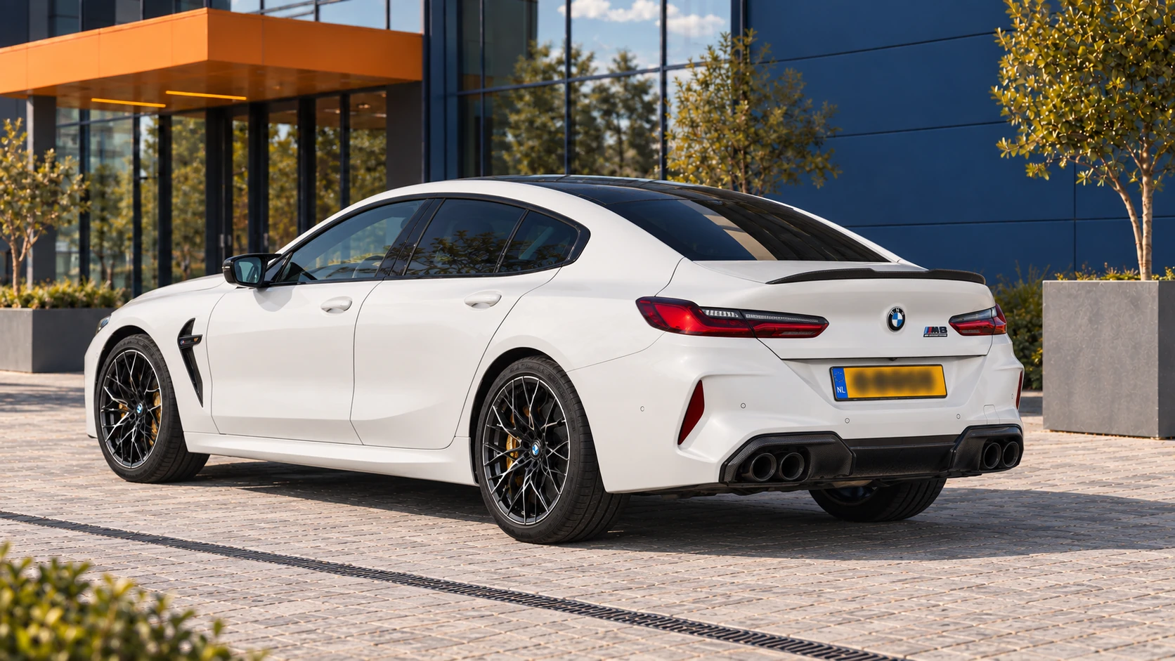 Achterzijde van dezelfde witte BMW M8 Competition Gran Coupé met vier uitlaatpijpen