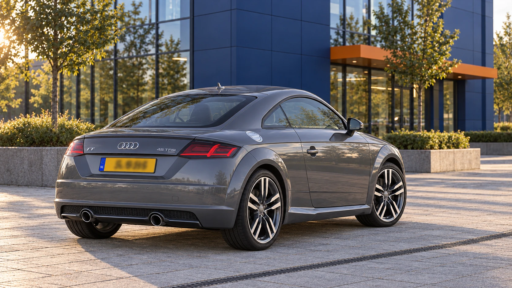 Grijze Audi TT 45 TFSI Coupé facelift van schuin achter, met twee ronde uitlaten en geel Nederlands kenteken