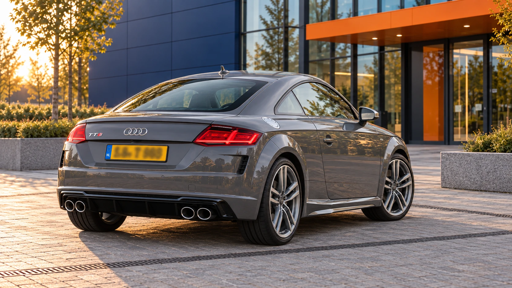 Grijze Audi TTS Coupé van de laatste 8S-generatie, schuin van achteren gezien met vier ronde uitlaateindstukken
